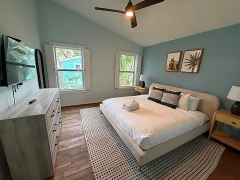 Blue bedroom with a made bed, folded towels and wood floors