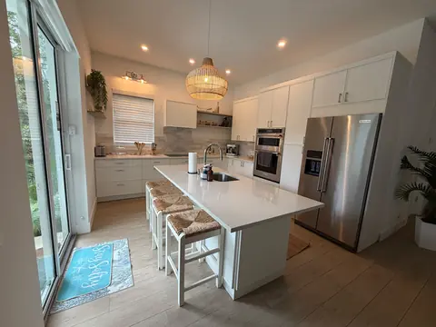 White kitchen with a clean island, woven stools and stainless steel appliances