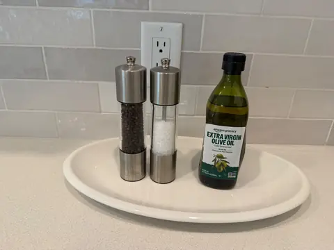 Salt and pepper mills and olive oil arranged on a tray on a kitchen counter