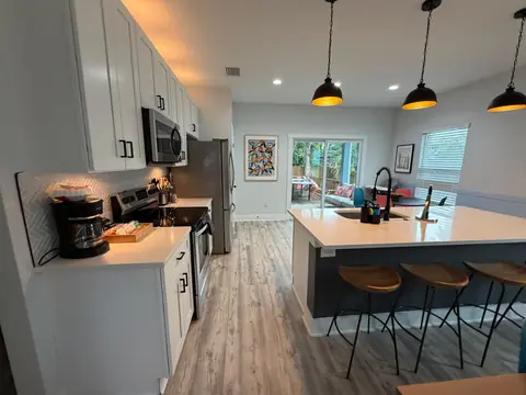 Kitchen with a blue island, white counters, black pendant lights and wood stools