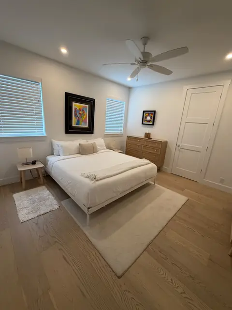 White bedroom with a neatly made bed, neutral rugs and a wooden dresser