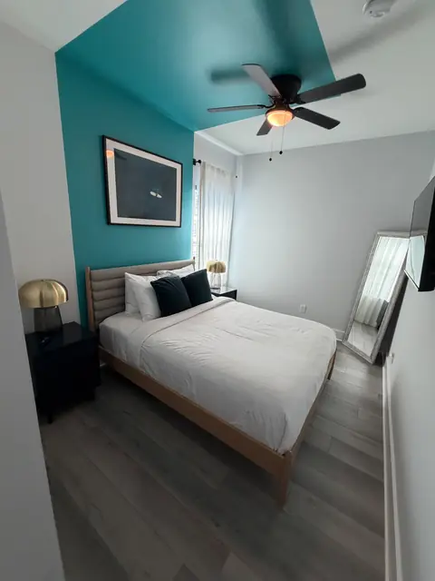 Bedroom with a teal accent wall, white bedding and matching bedside lamps